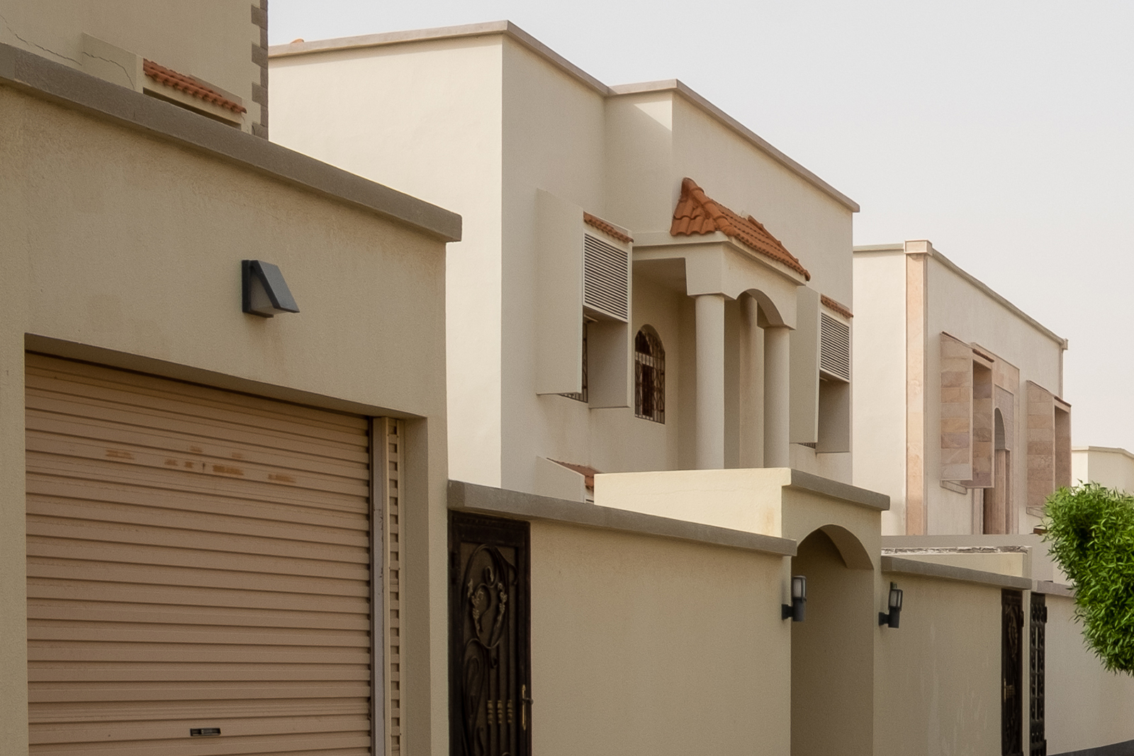 Private Villa with Modern Beige Exterior Finish Modern villa exterior with beige walls, arched windows, and decorative roofing tiles in Bahrain.